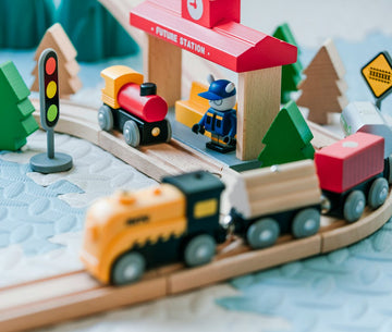 Wooden toy train set with a red station, trains and trees on a play mat